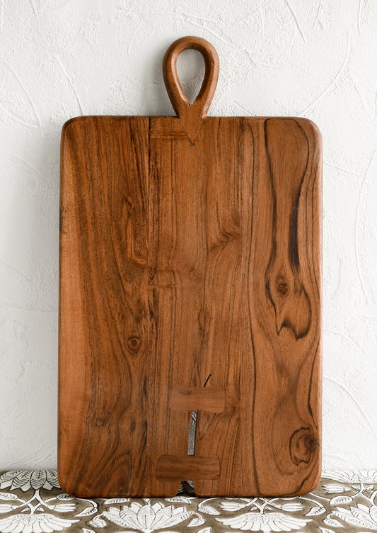 A rectangular cutting board with loop handle at top and bowtie inlay detailing.