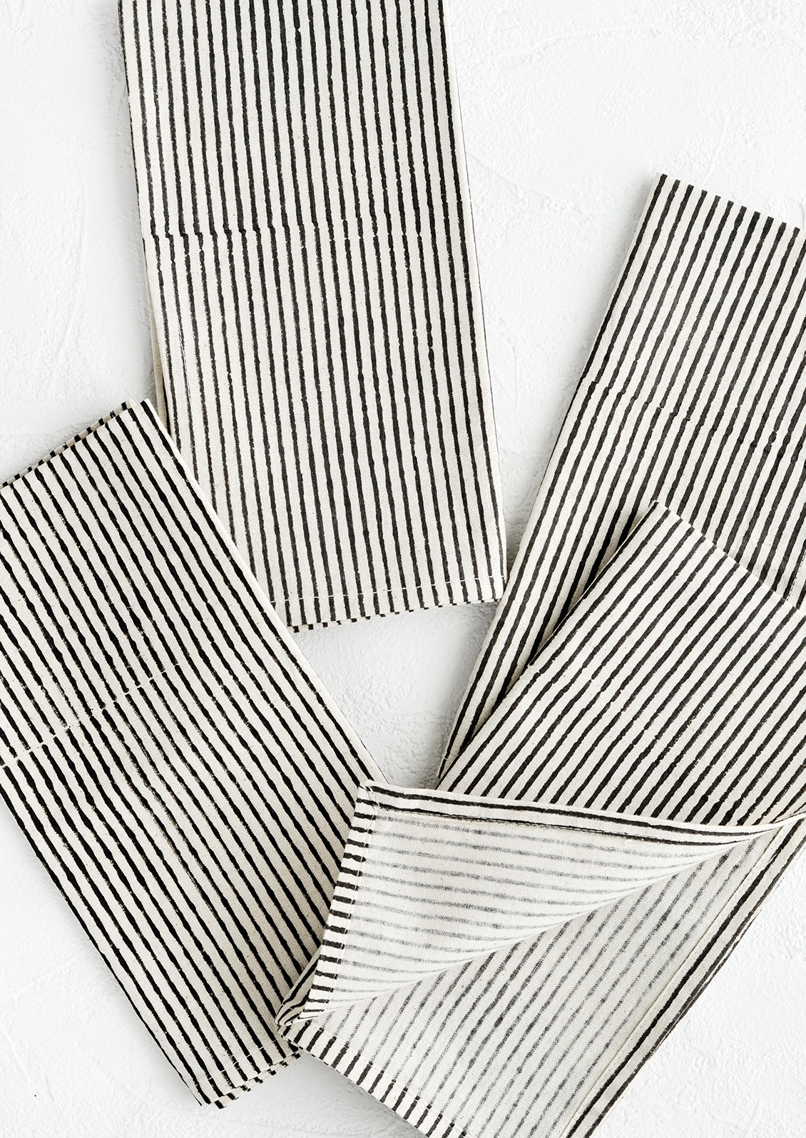 Scattered folded fabric napkins in natural cotton with hand-drawn line pattern in black.