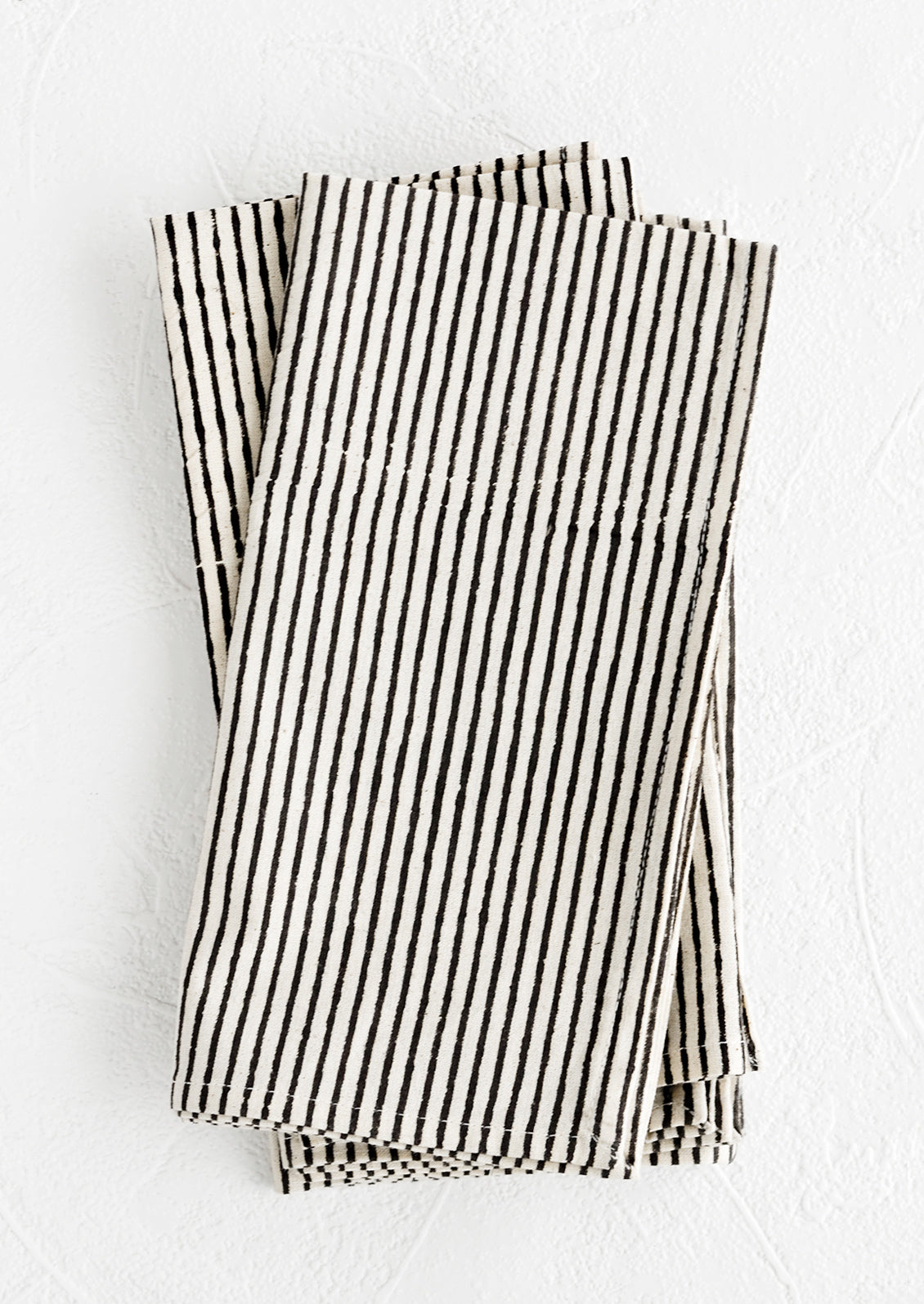 A stack of folded fabric napkins in natural cotton with hand-drawn line pattern in black.
