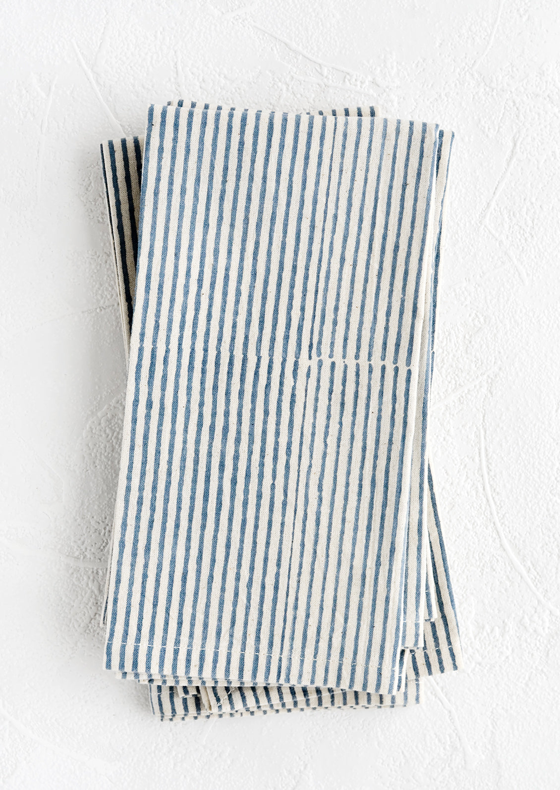 A stack of folded fabric napkins in natural cotton with hand-drawn line pattern in indigo.