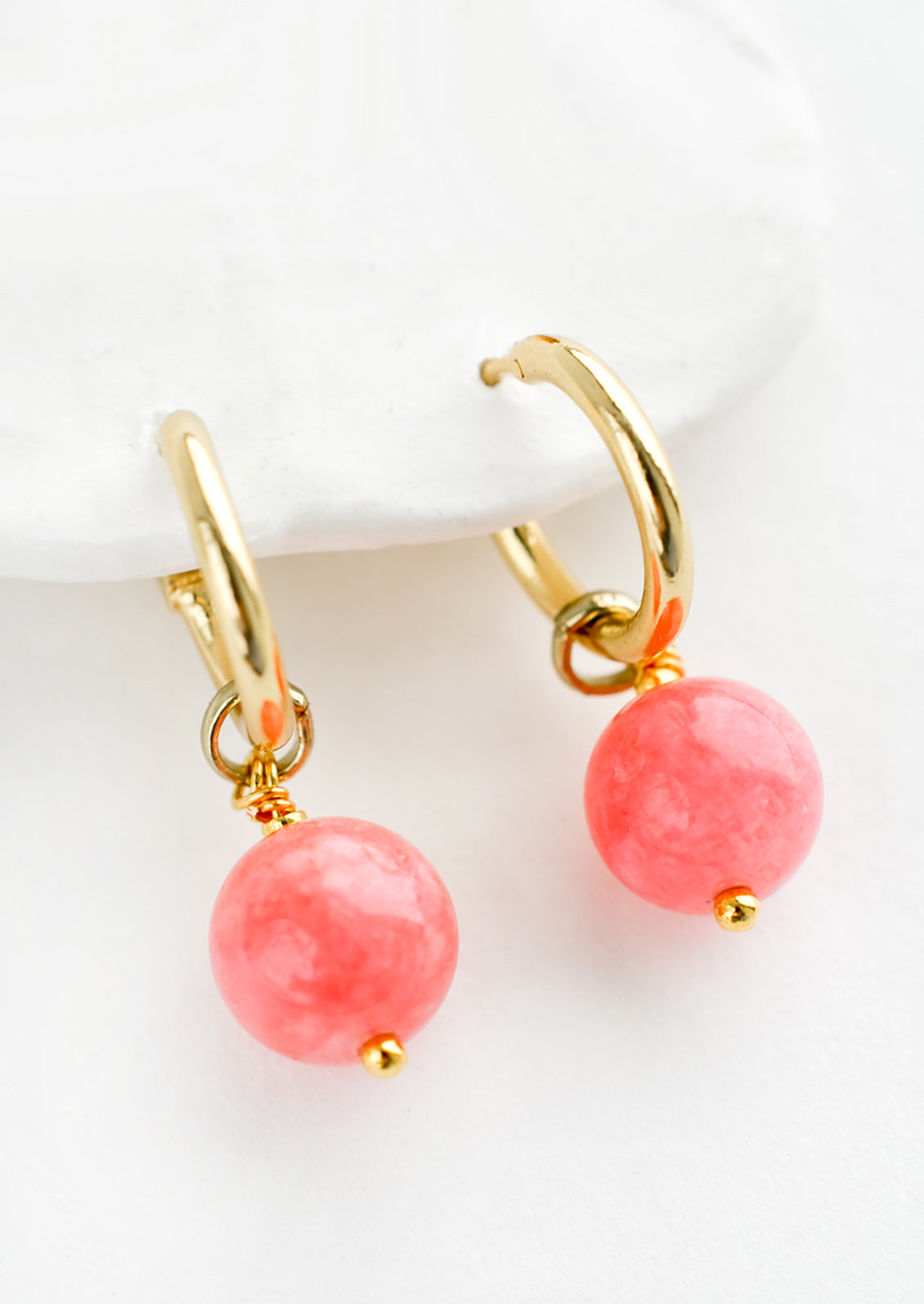 A pair of gold hoop earrings with pink spherical stones.