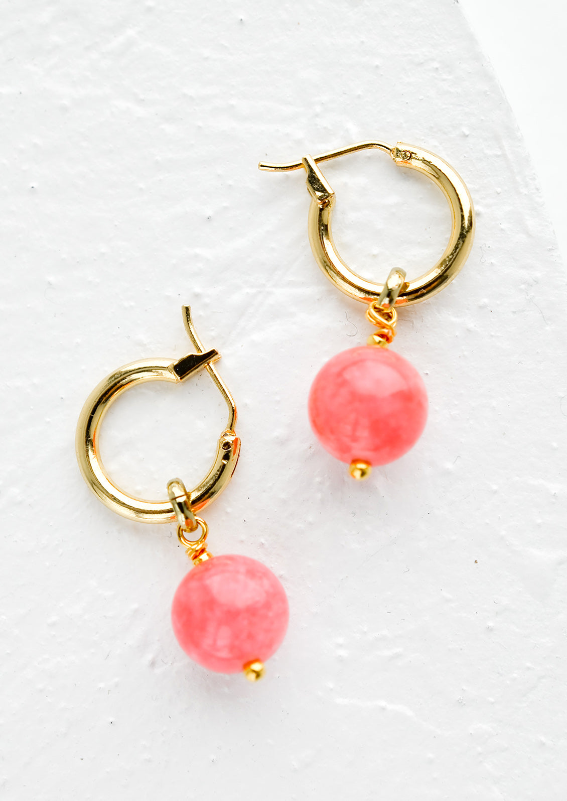 A pair of gold hoop earrings with pink spherical stones.
