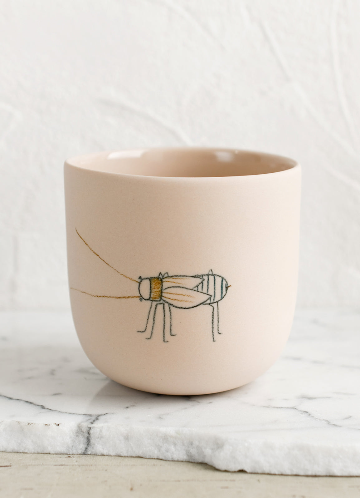 A large pastel orange porcelain cup with beetle sketch.