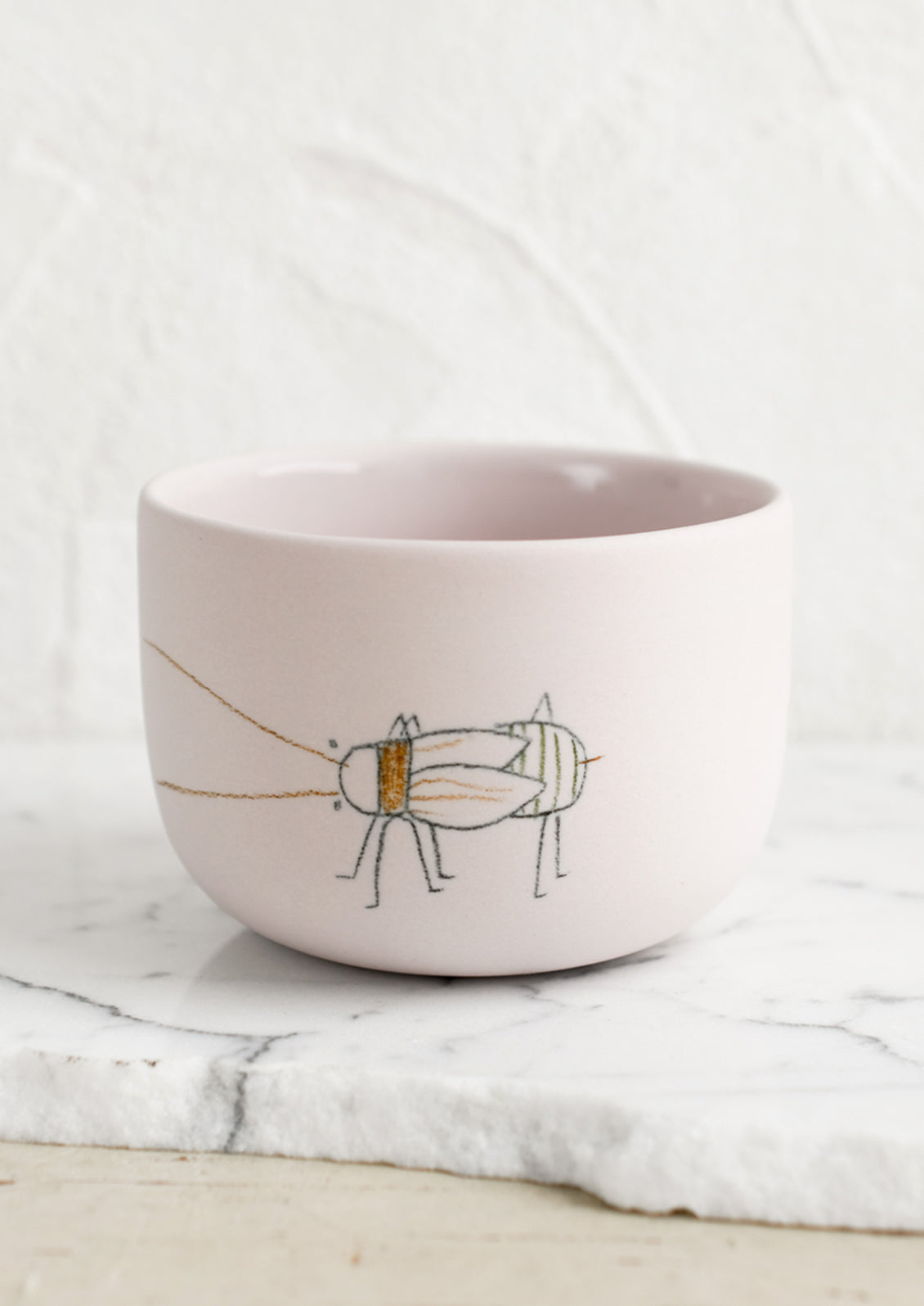 A short and wide pink porcelain cup with beetle sketch.