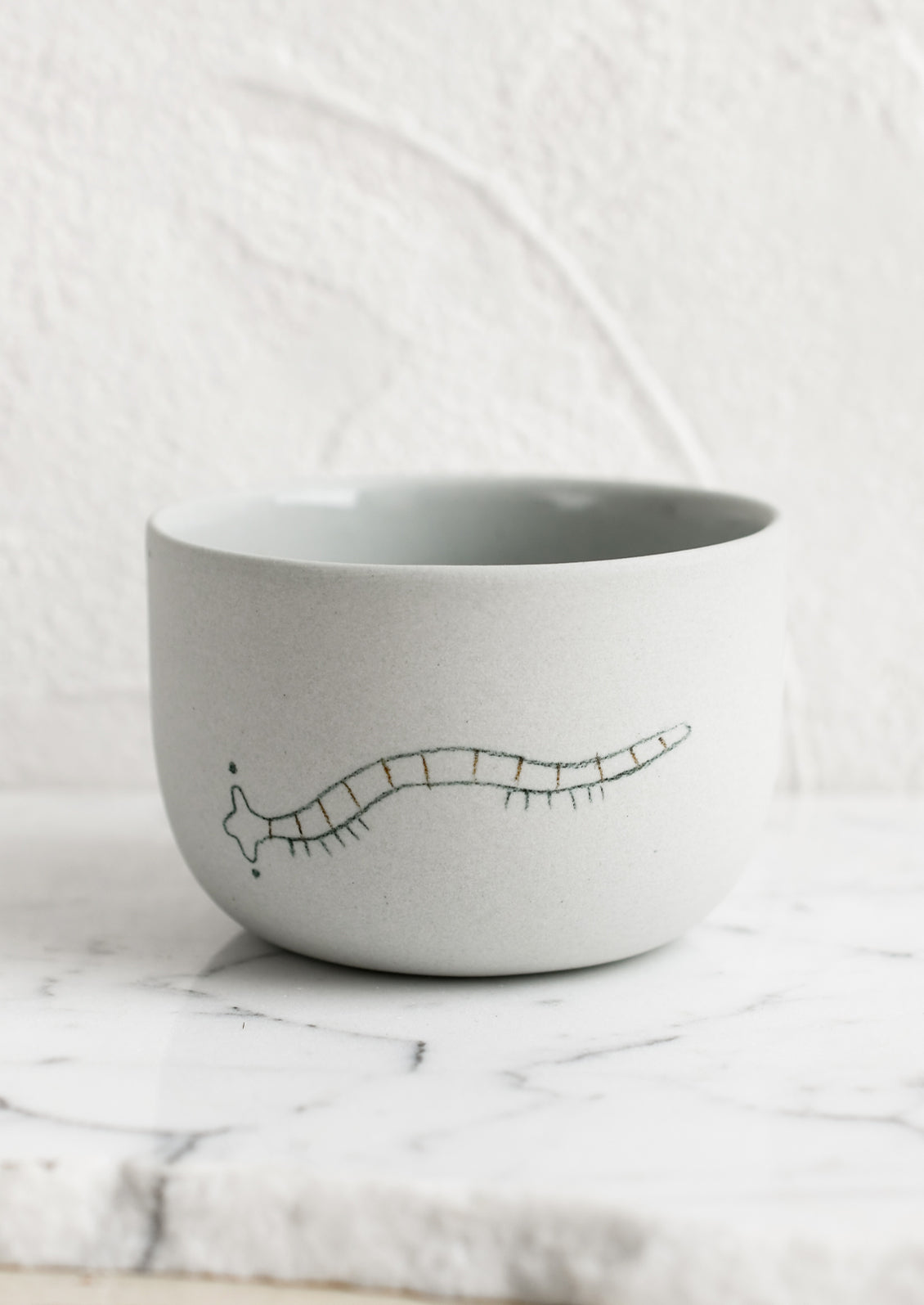 A short and wide grey porcelain cup with millipede sketch.