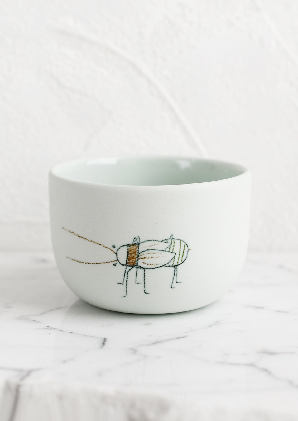 A short and wide mint porcelain cup with beetle sketch.