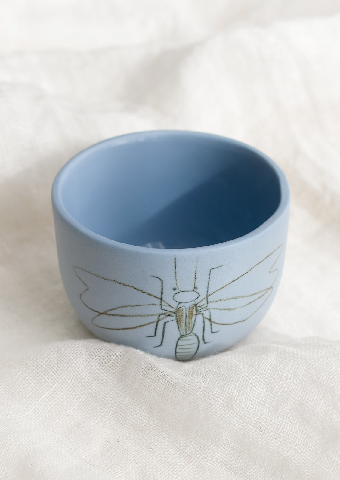 A short and wide periwinkle blue cup with firefly sketch.