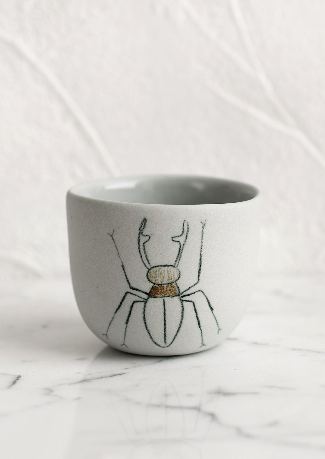 An extra small grey porcelain cup with beetle sketch.