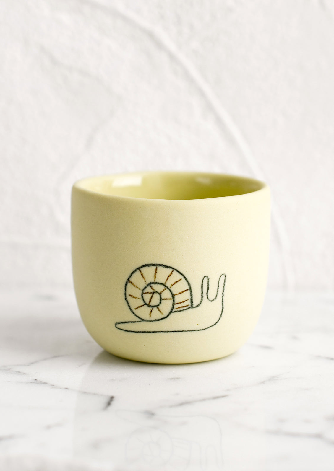 An extra small yellow porcelain cup with snail sketch.