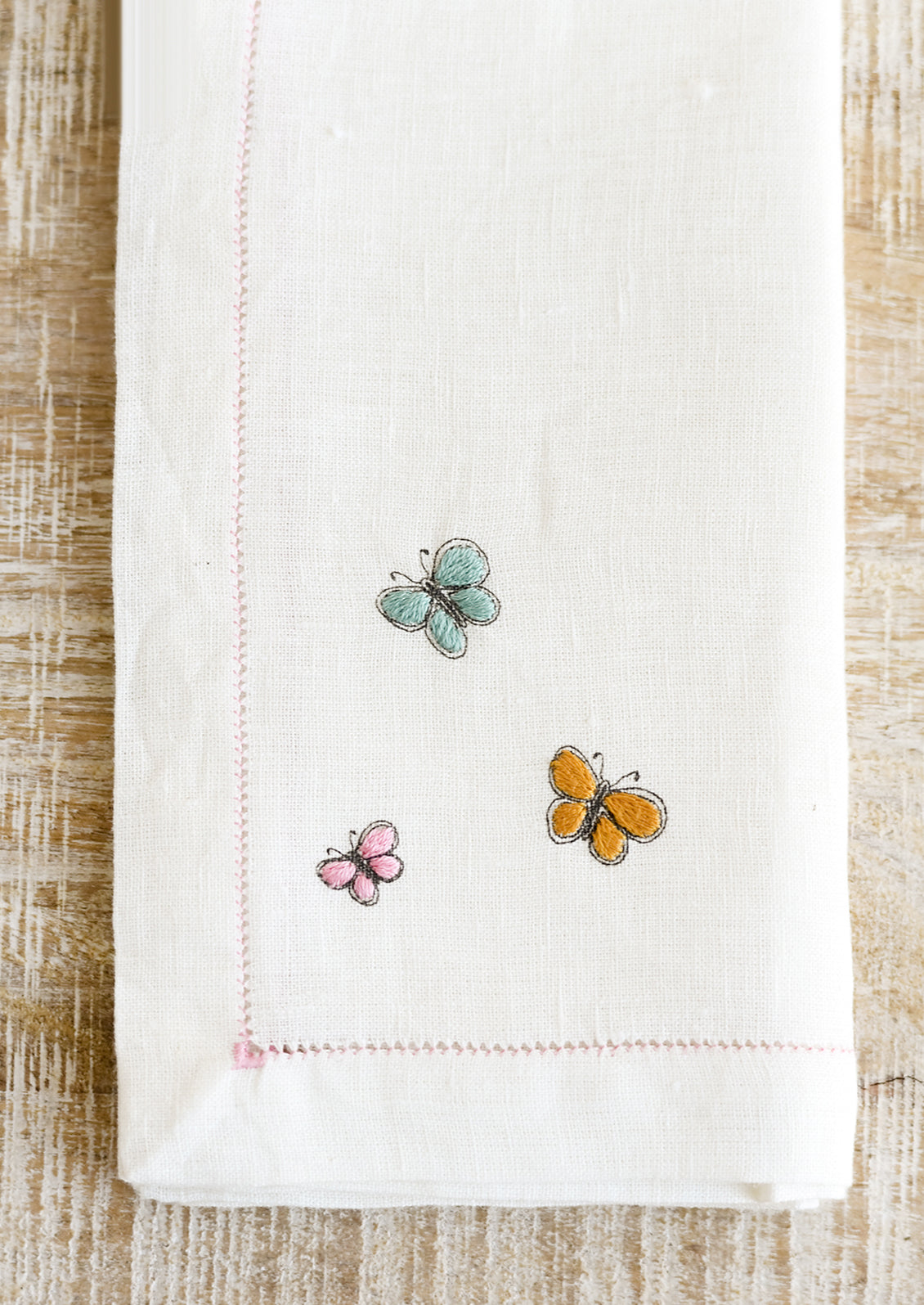Butterfly embroidery detailing on a white linen napkin.