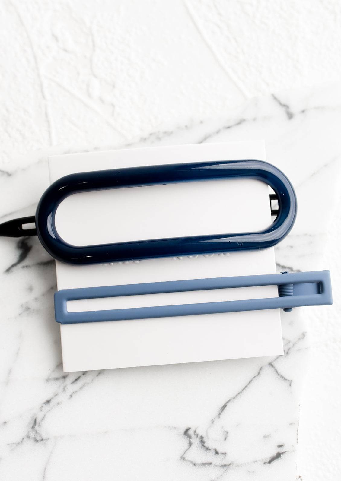 A pair of hair clips in oval and rectangular shapes in shades of denim blue.