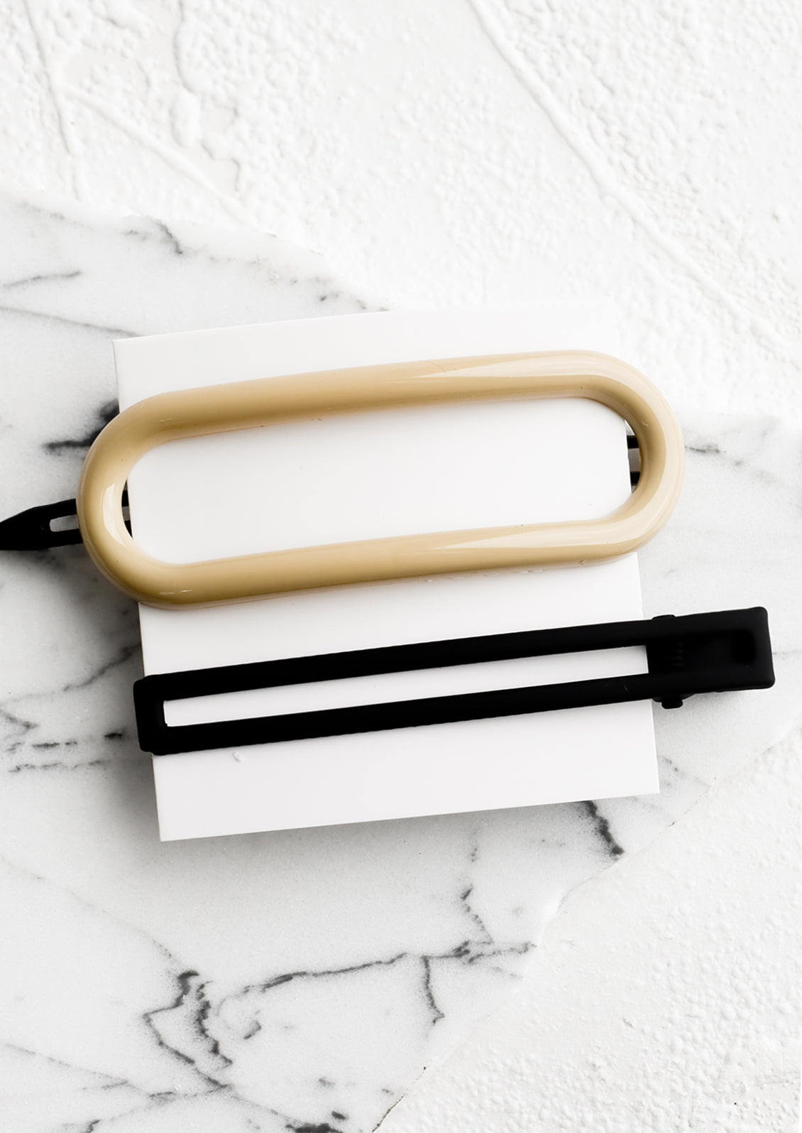 A pair of hair clips in oval and rectangular shapes in ivory and black.