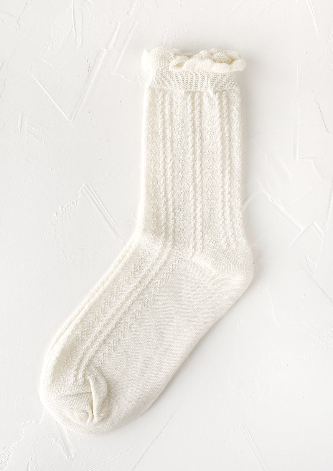 A pair of cable knit socks with ruffled ankle in white.
