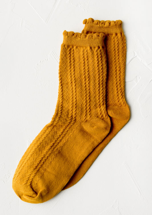 A pair of cable knit socks with ruffled ankle in amber.