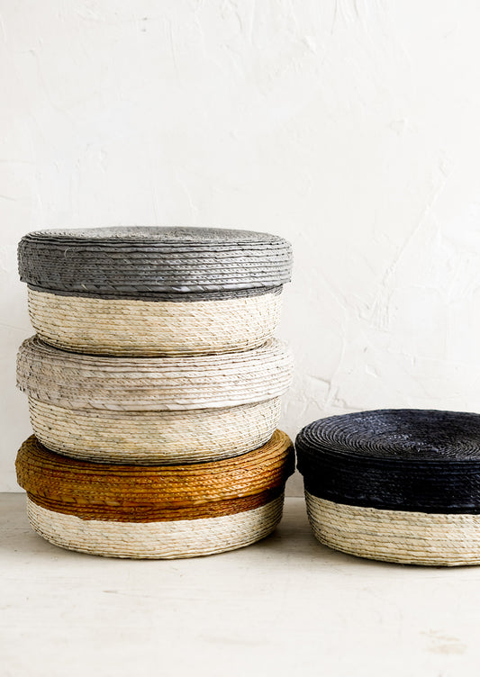 Shallow, round palm leaf storage baskets stacked in different colors.