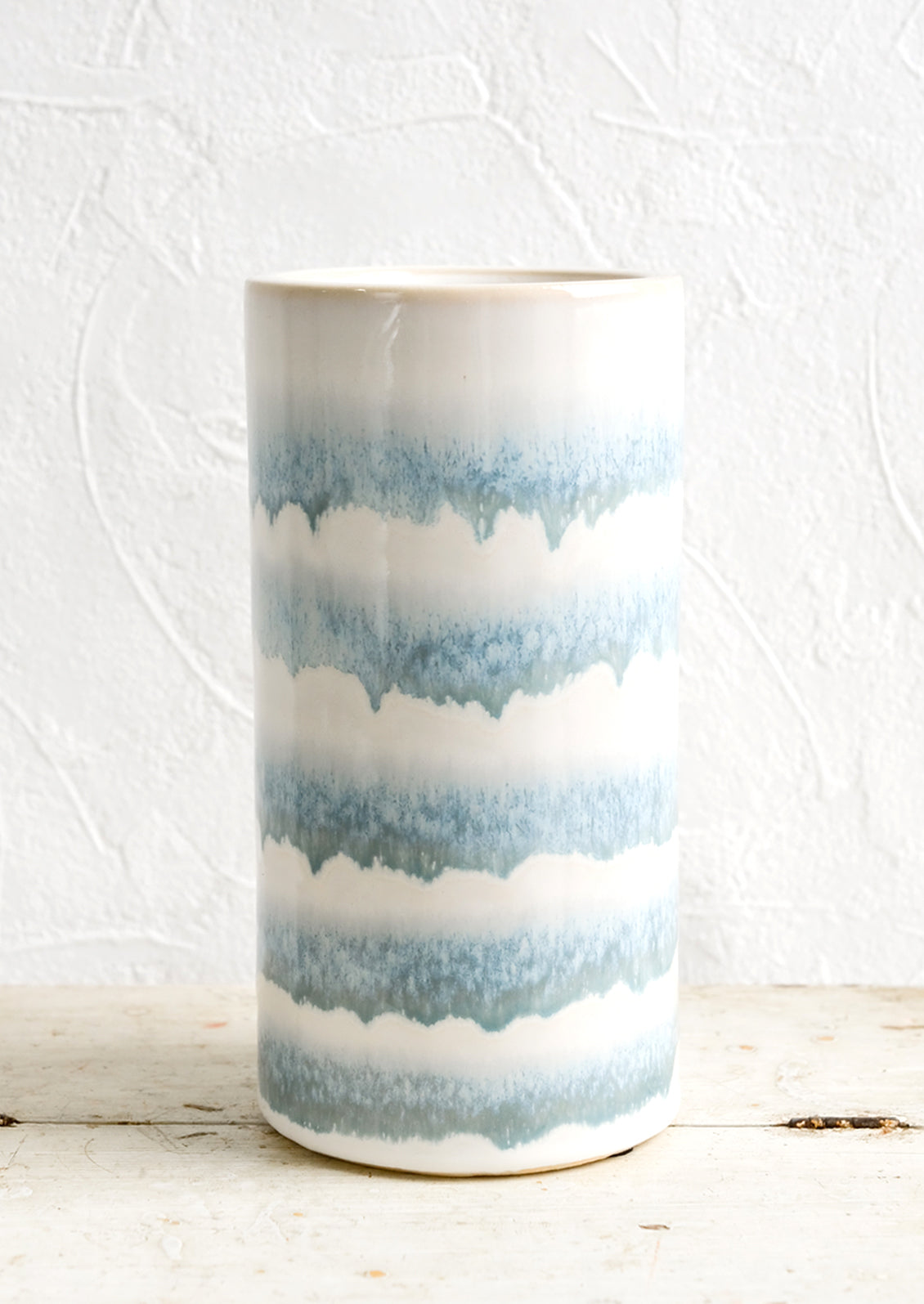A tall cylindrical ceramic vase with blue and white stripes.