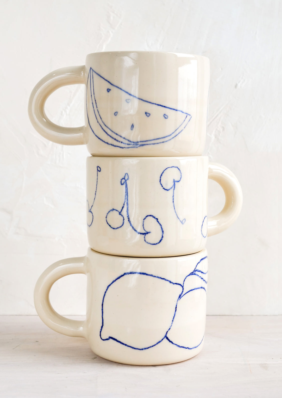 A stack of three ceramic mugs with fruit line drawings.