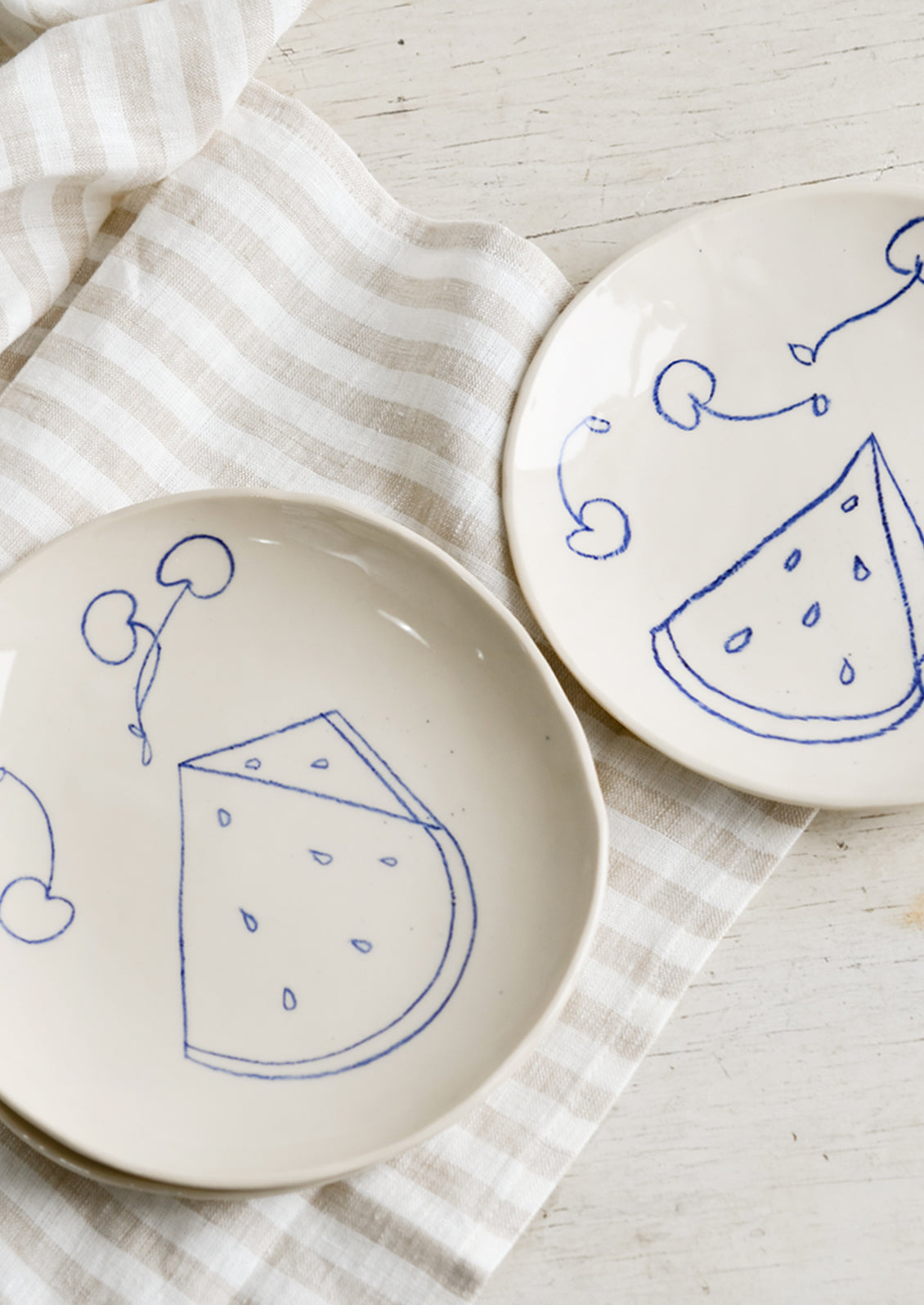Two ceramic side plates with still life fruit drawings in blue.