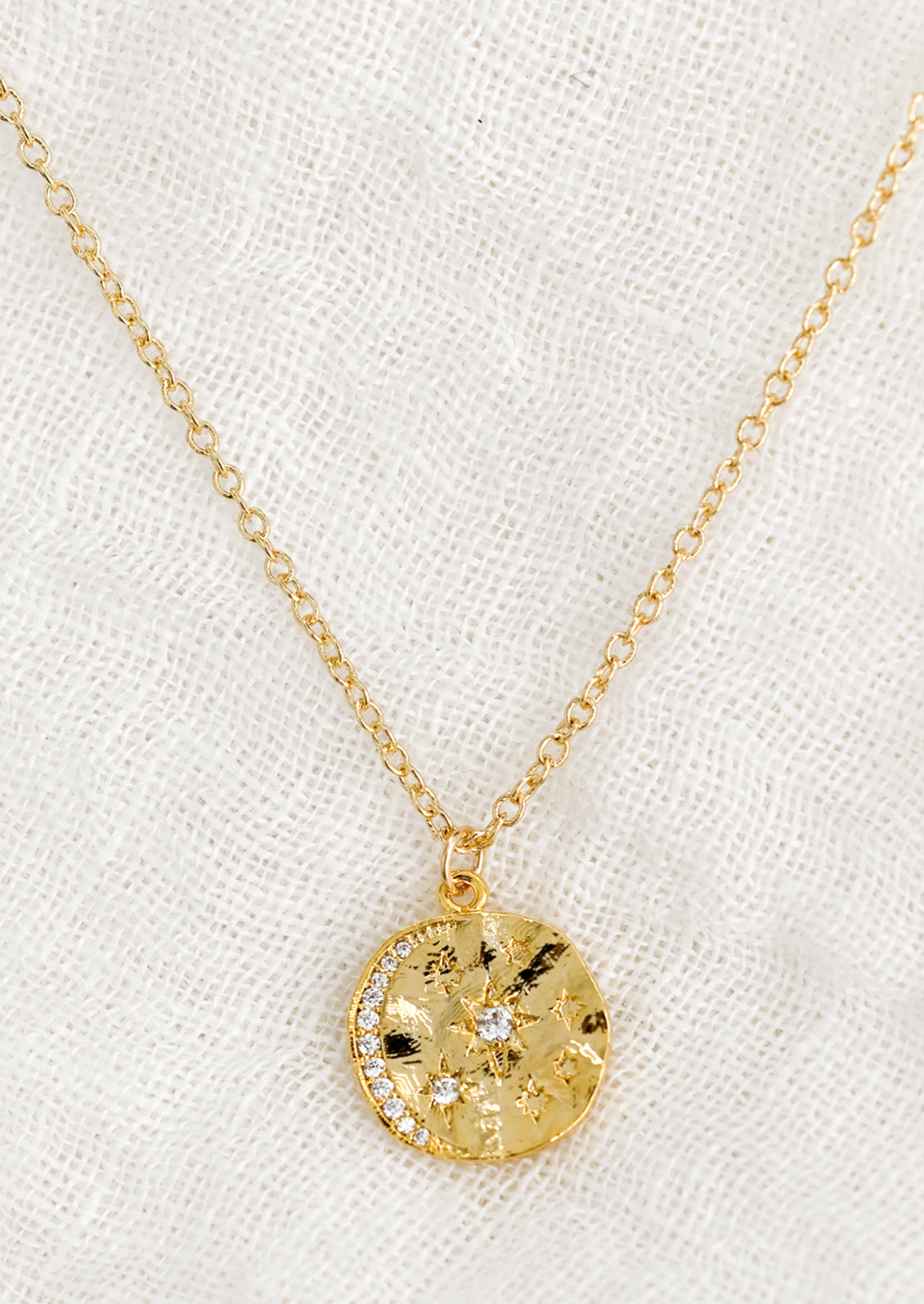 A round pendant necklace with moon and star crystal design.