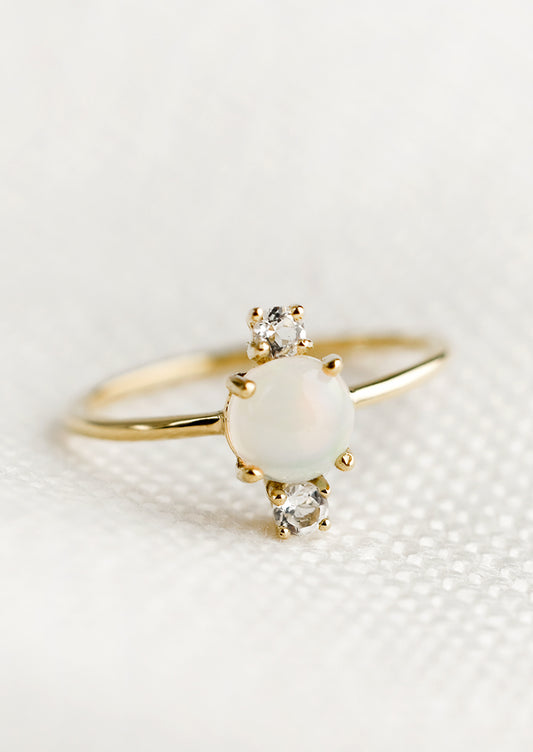 A gold ring with large center opal stone and two small white topaz stones.