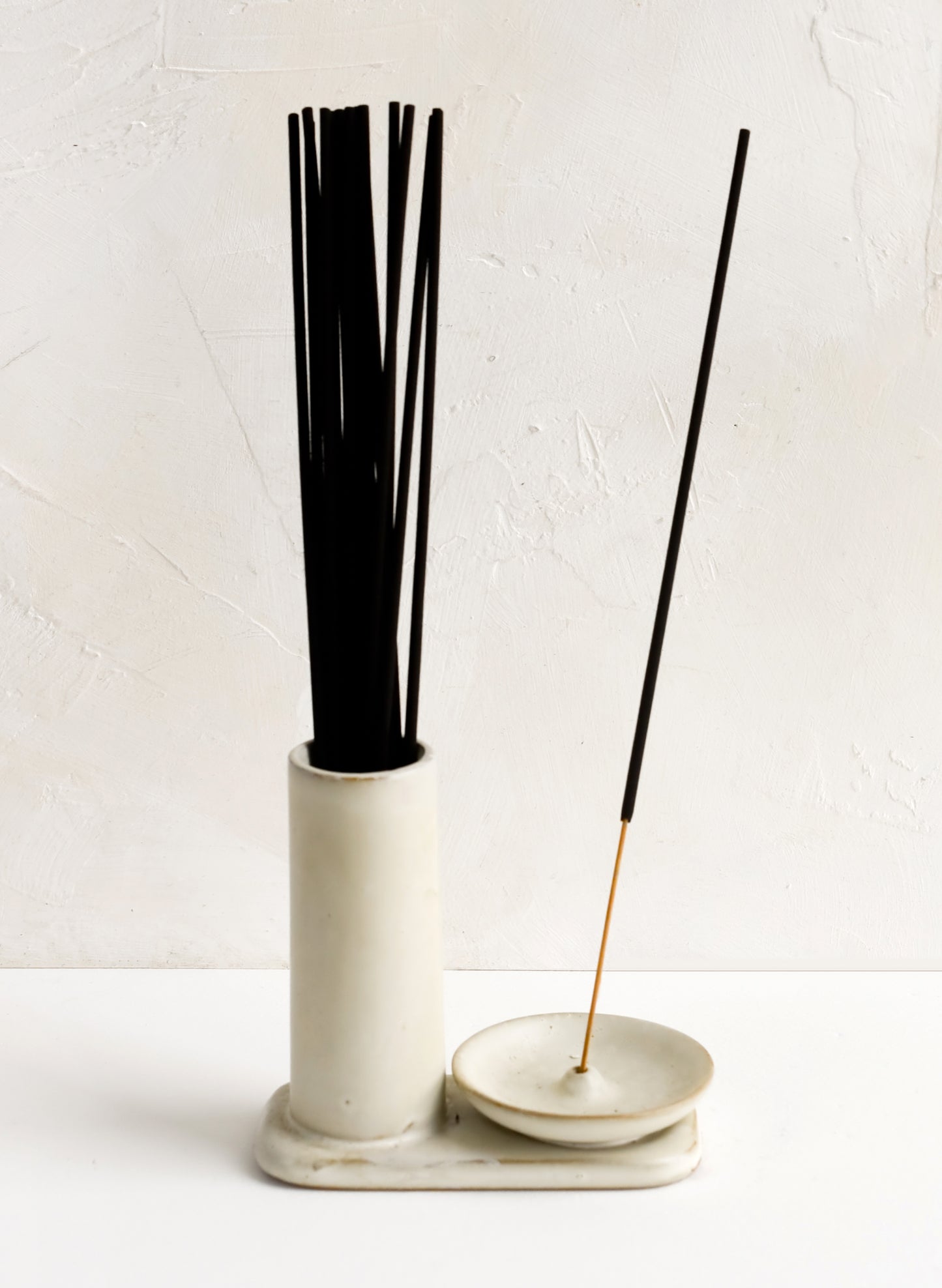 A tan ceramic incense holder with stand and incense holder, holding incense sticks.