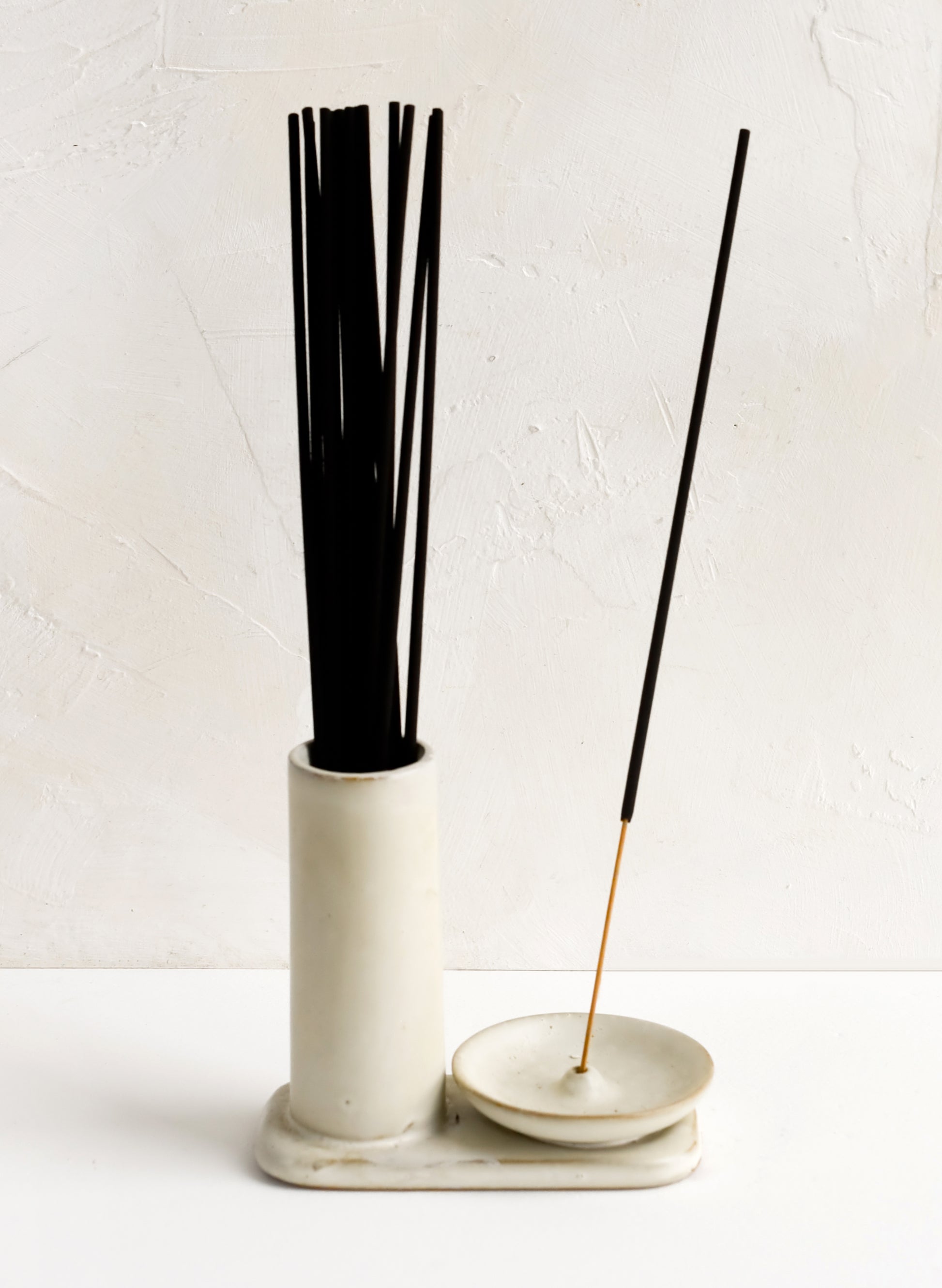 A tan ceramic incense holder with stand and incense holder, holding incense sticks.