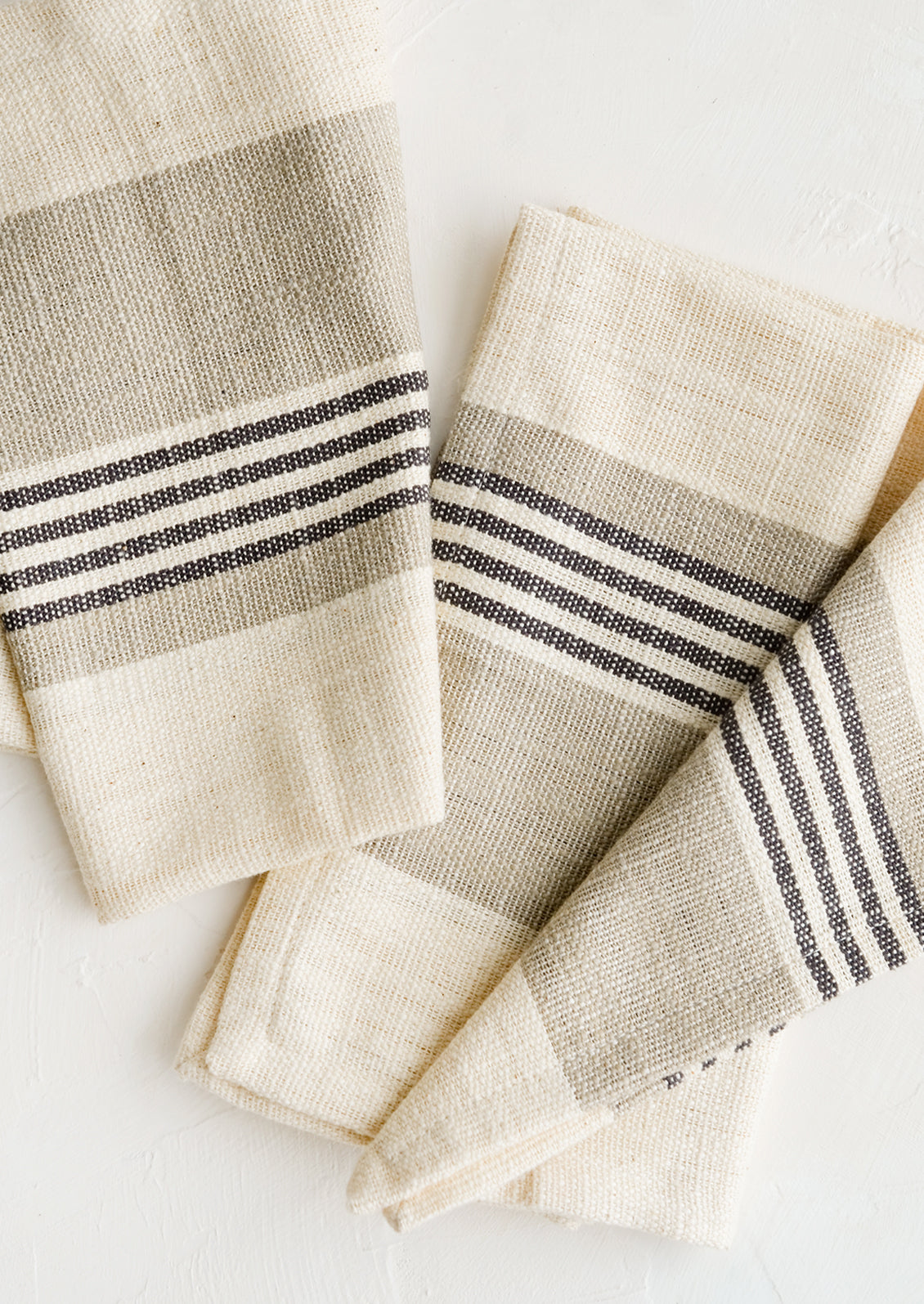 A pair of folded napkins in ivory with black and tan striped band across middle.