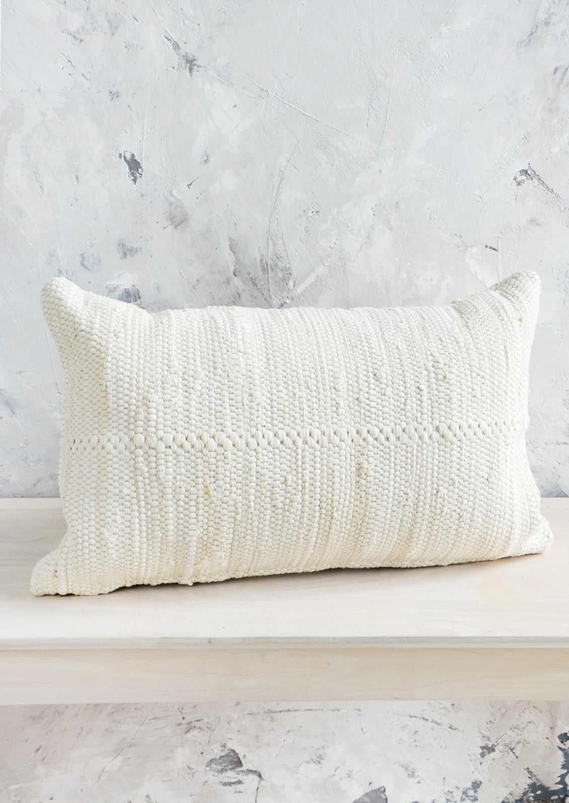 A lumbar throw pillow made from cream colored cotton chindi fabric.