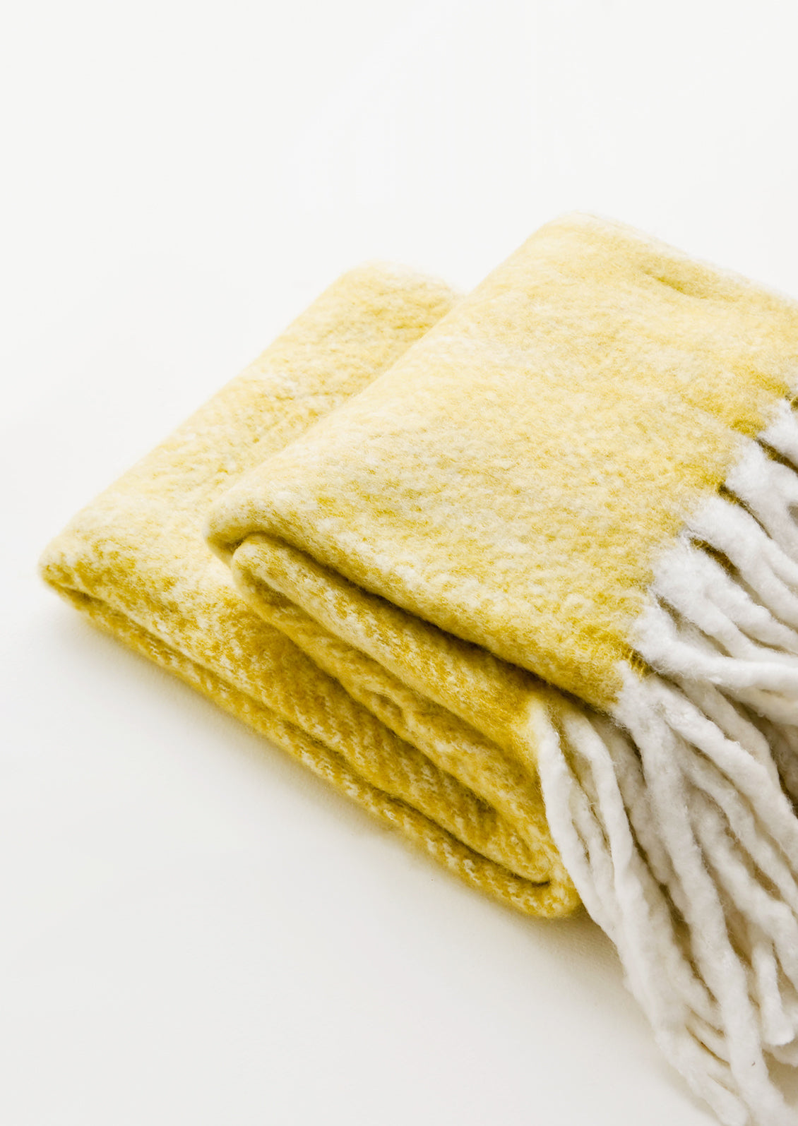 Plush and wooly yellow throw blanket with exaggerated fringe trim in ivory