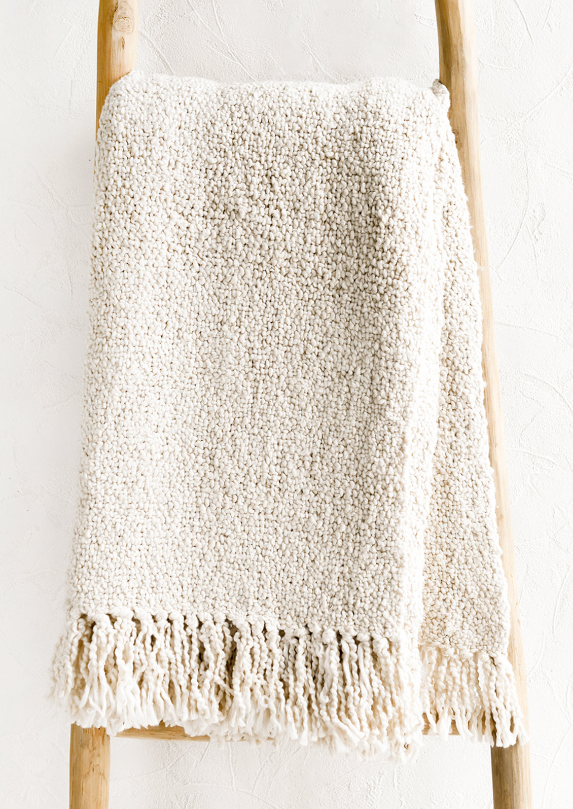 An ivory colored cotton throw with chunky boucle texture.