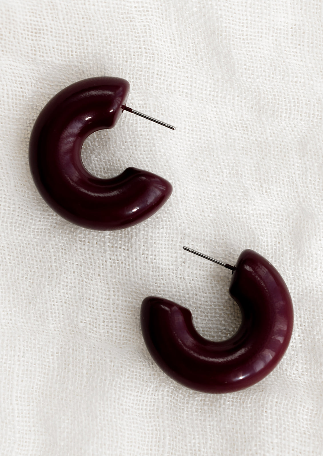 A pair of chunky gloss finish hoop earrings in raisin purple-brown.