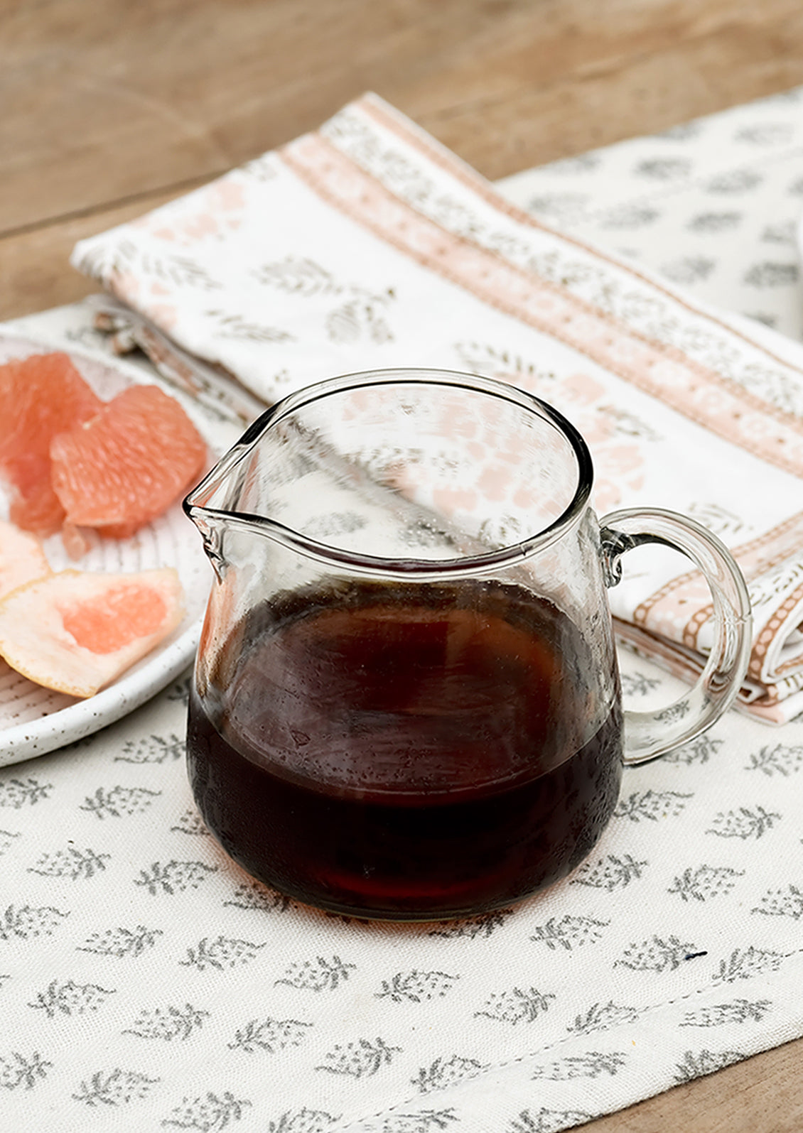 A small glass pitcher on a table, filled with maple syrup.