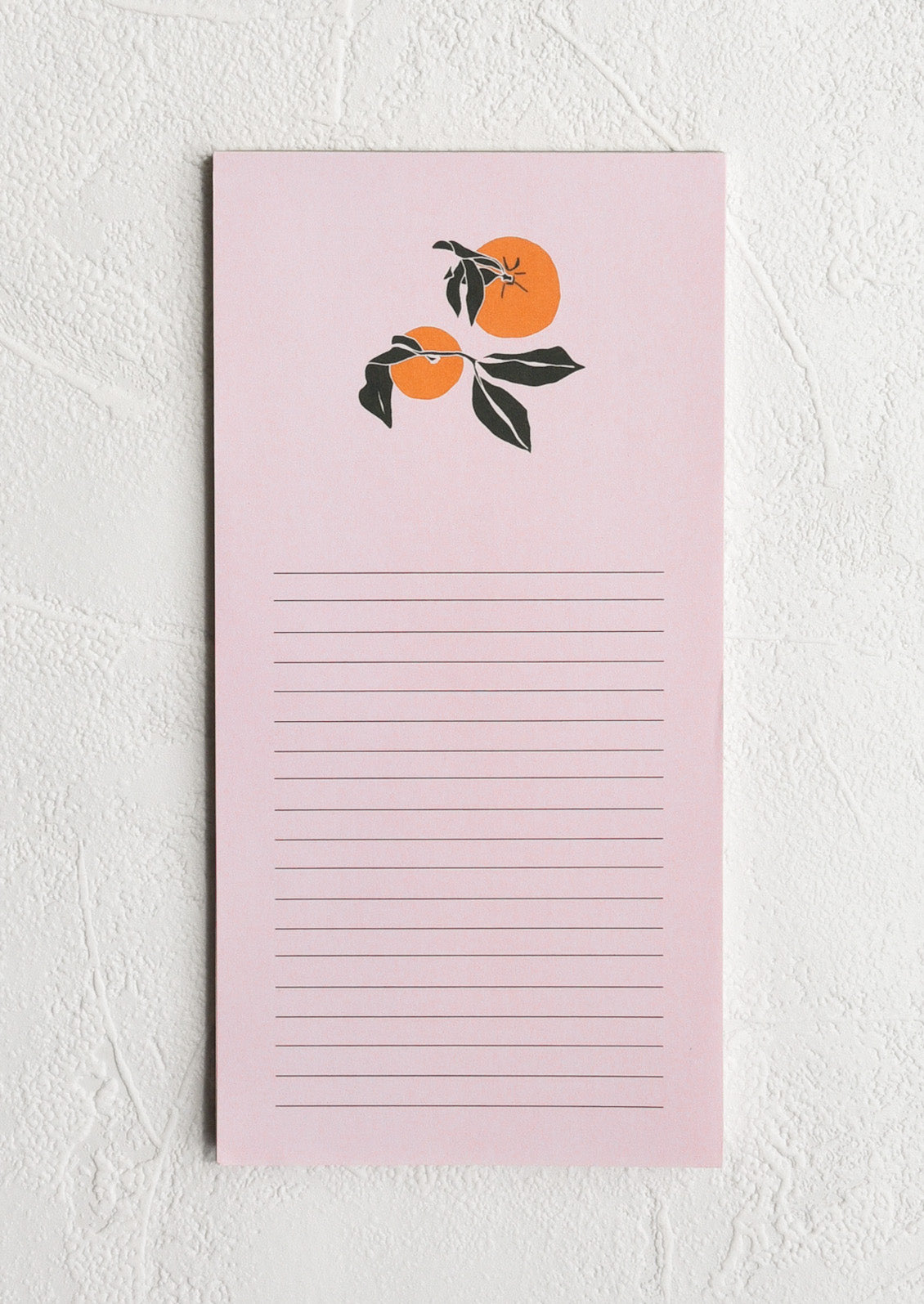 A light pink lined notepad with two oranges at the top
