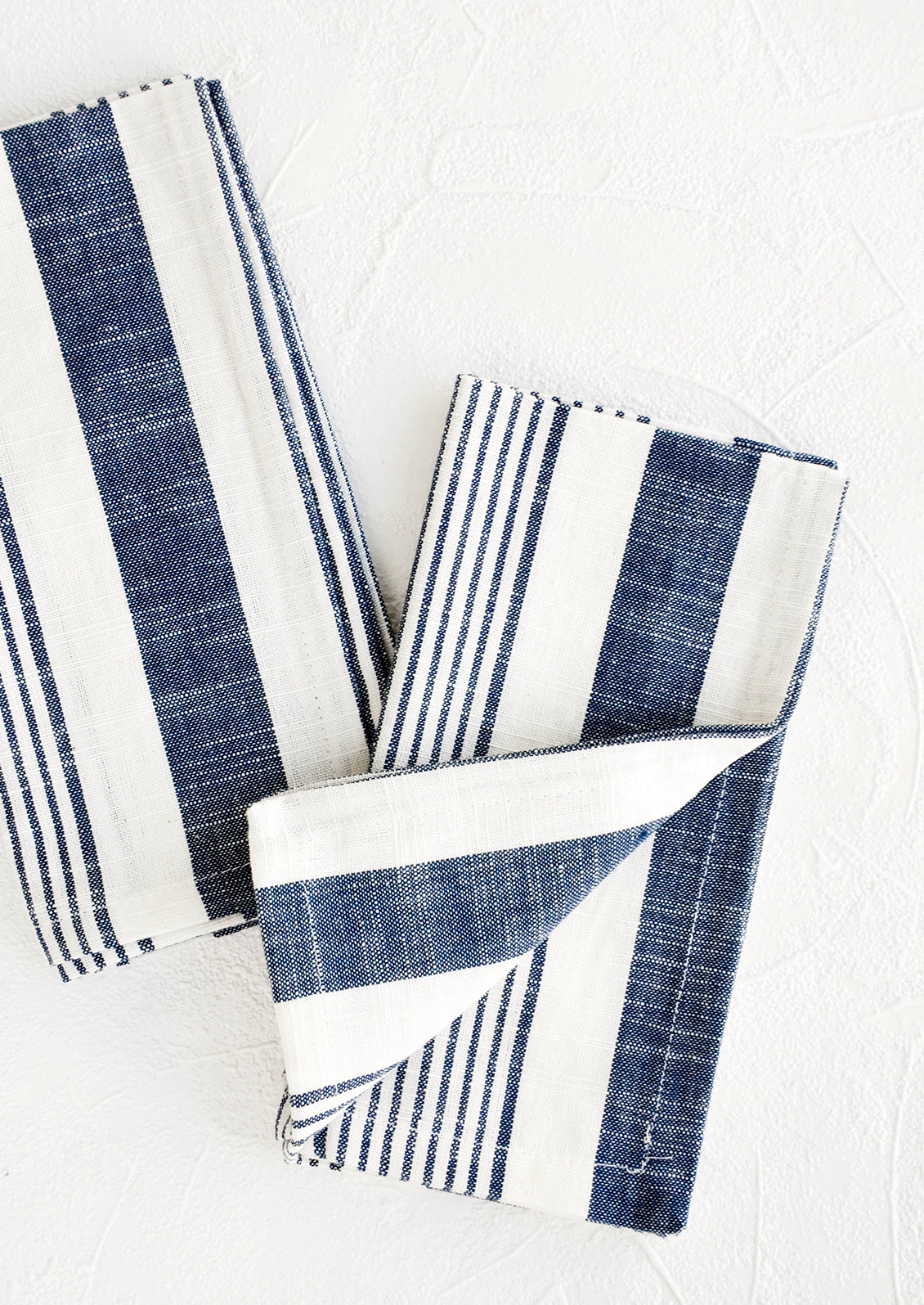 White and blue striped cotton napkins, pictured folded as a pair.