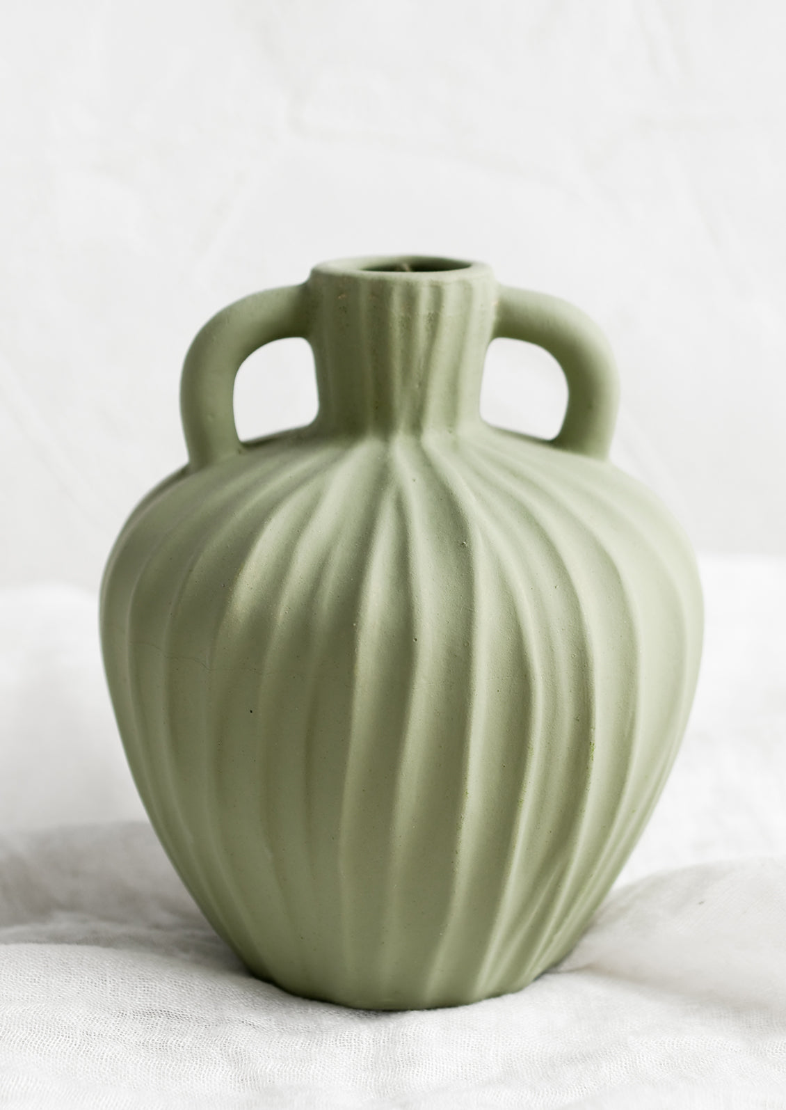 A mint green ceramic vase with handles at sides and carved line texture.