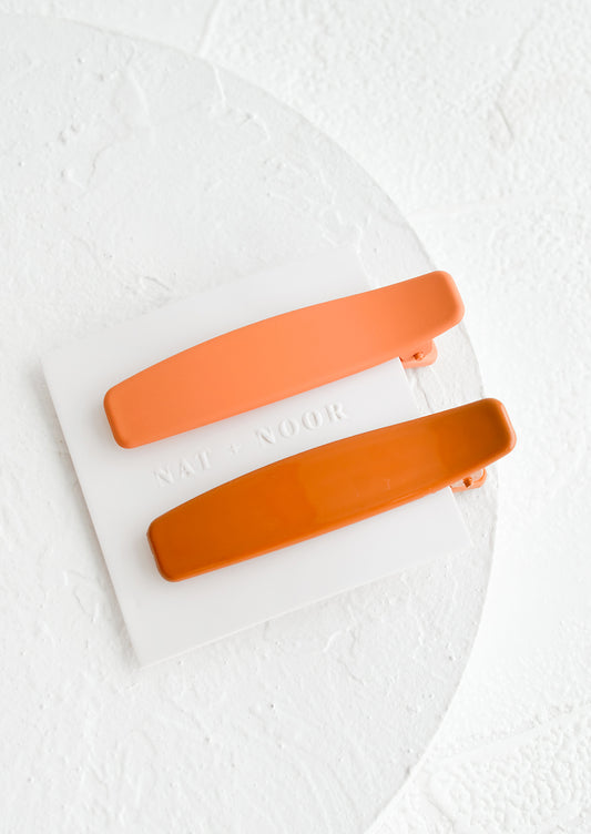 A pair of hair clips with one terracotta and one peach.