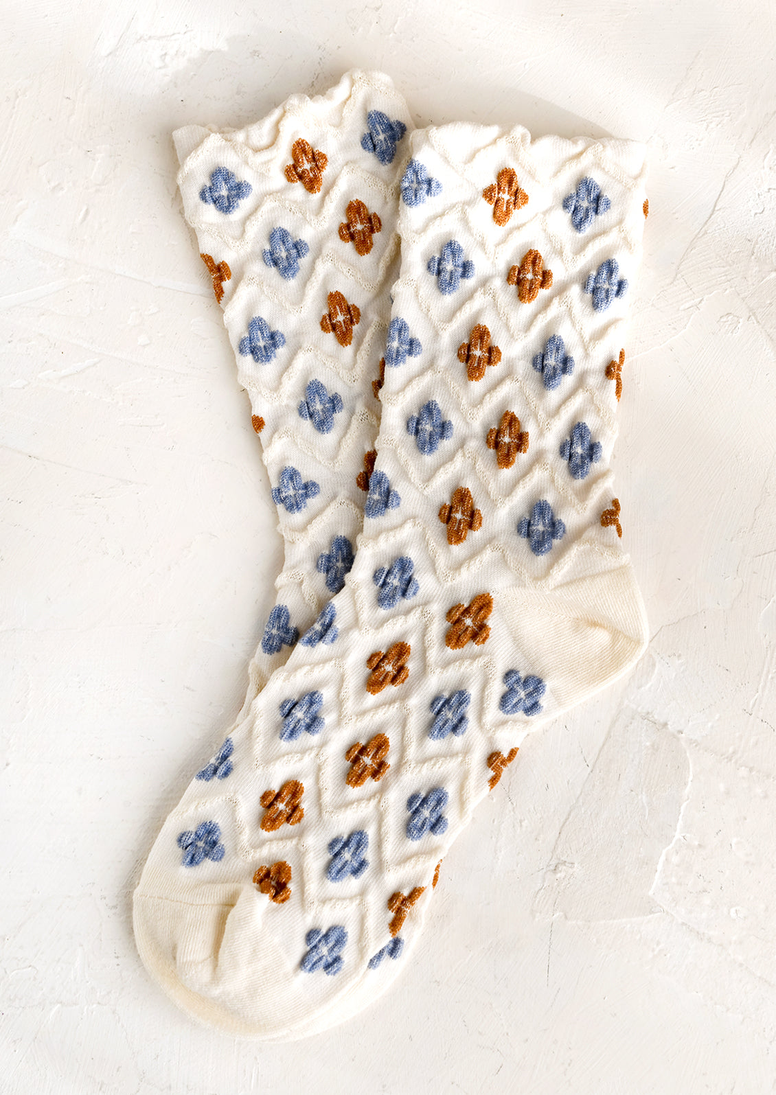 A pair of ivory socks with raised diamond texture and blue and brown clover shapes.