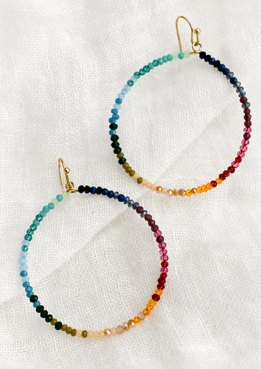 A pair of beaded hoop earrings in gradient rainbow colors.