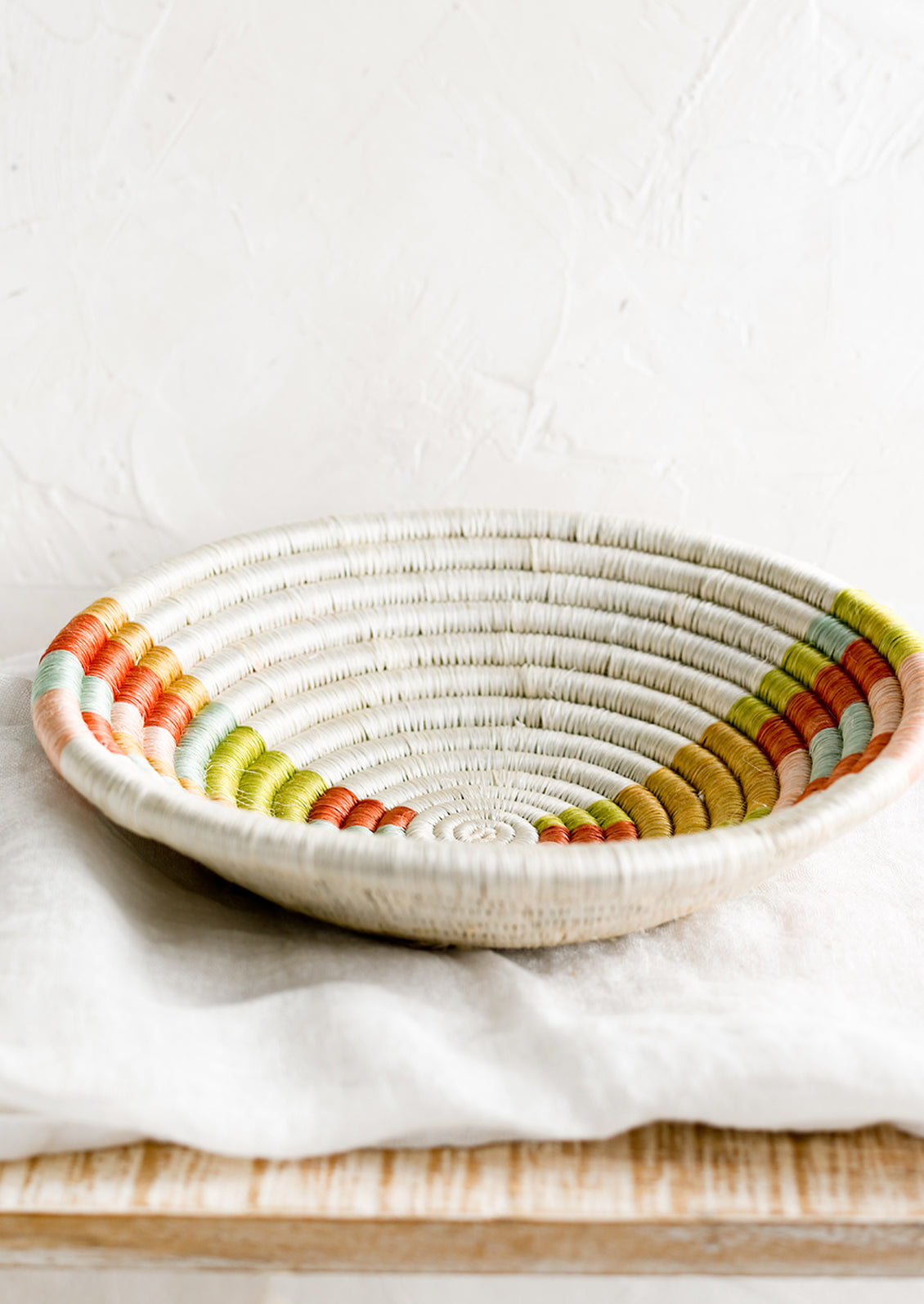 A woven sweetgrass bowl in white with multicolor geometric design.