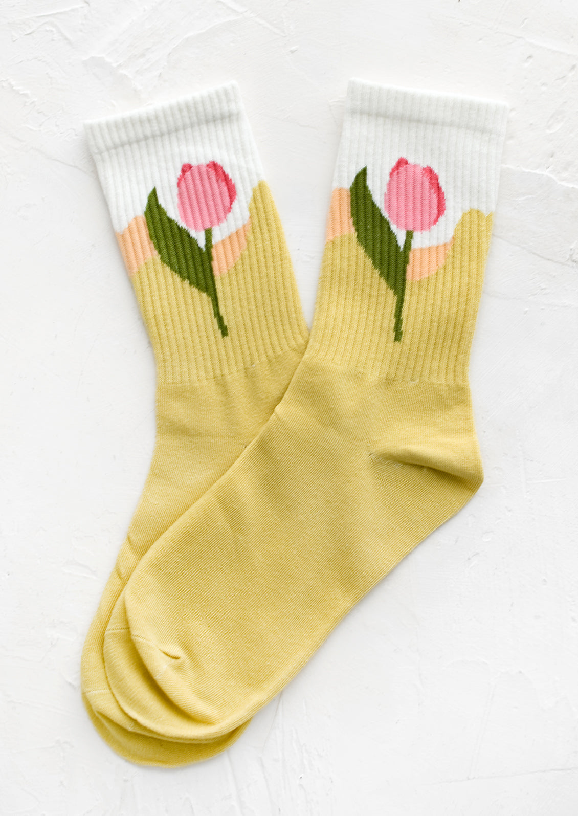 A pair of socks in yellow with pink tulip design at ankle.
