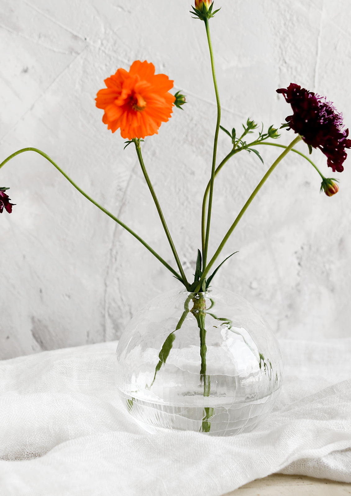 A clear crackled glass bud vase with flowers.