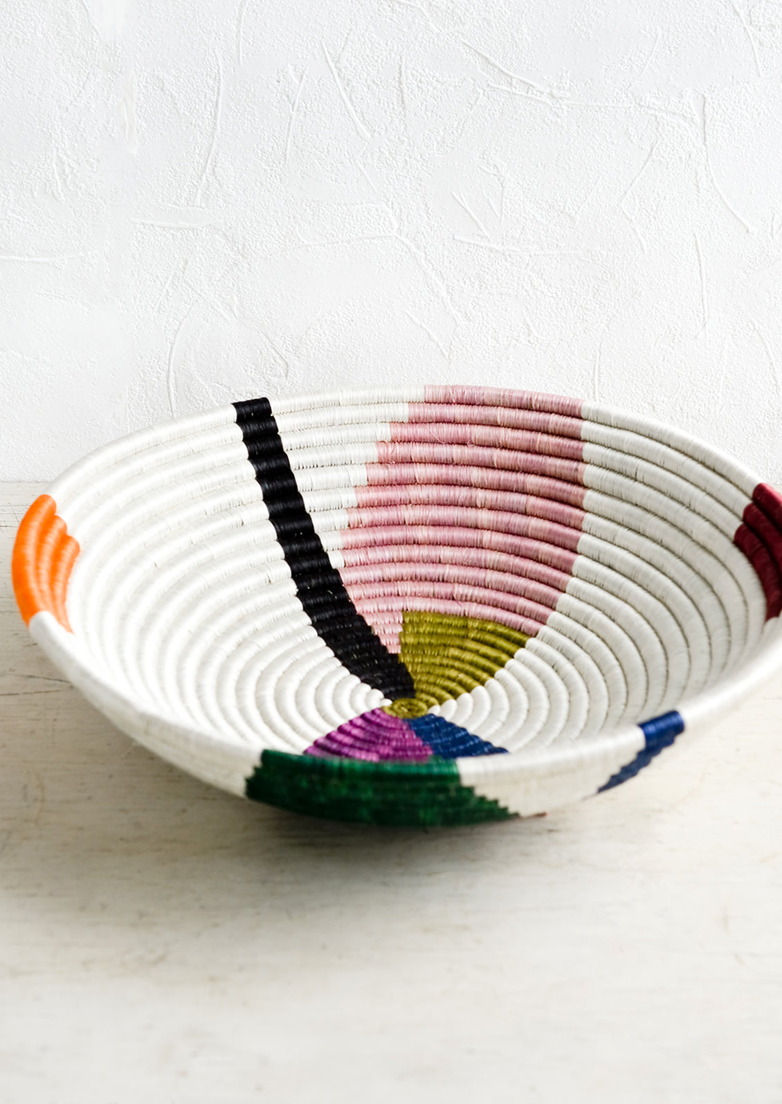 A large woven sweetgrass bowl in white with colorful abstract shapes.