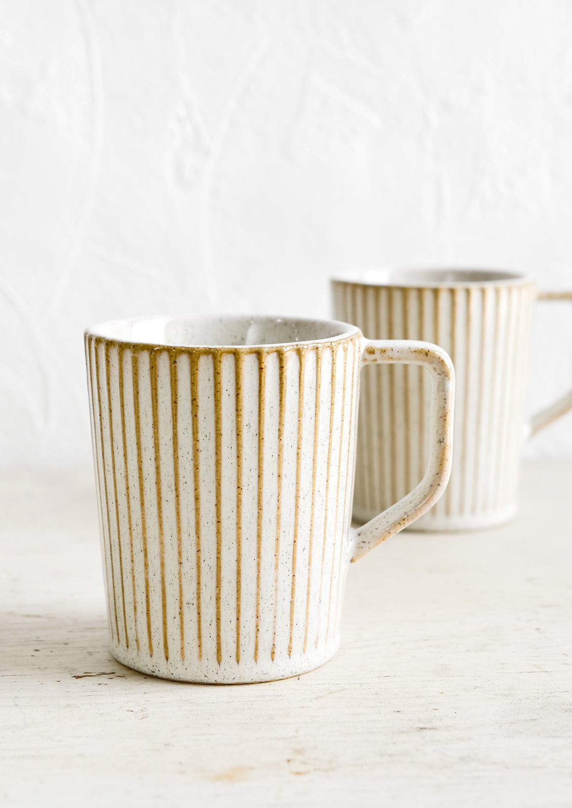 Two ceramic mugs in a glossy, neutral tan glaze with vertical grooved texture.
