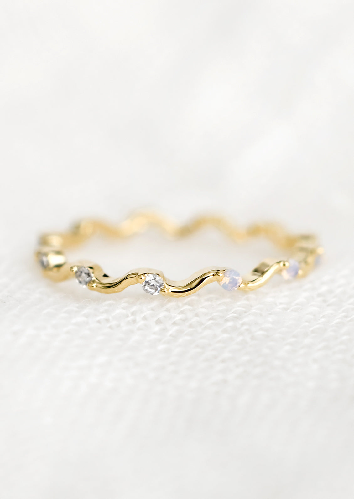 A gold squiggle shaped ring with crystal and opal stones.