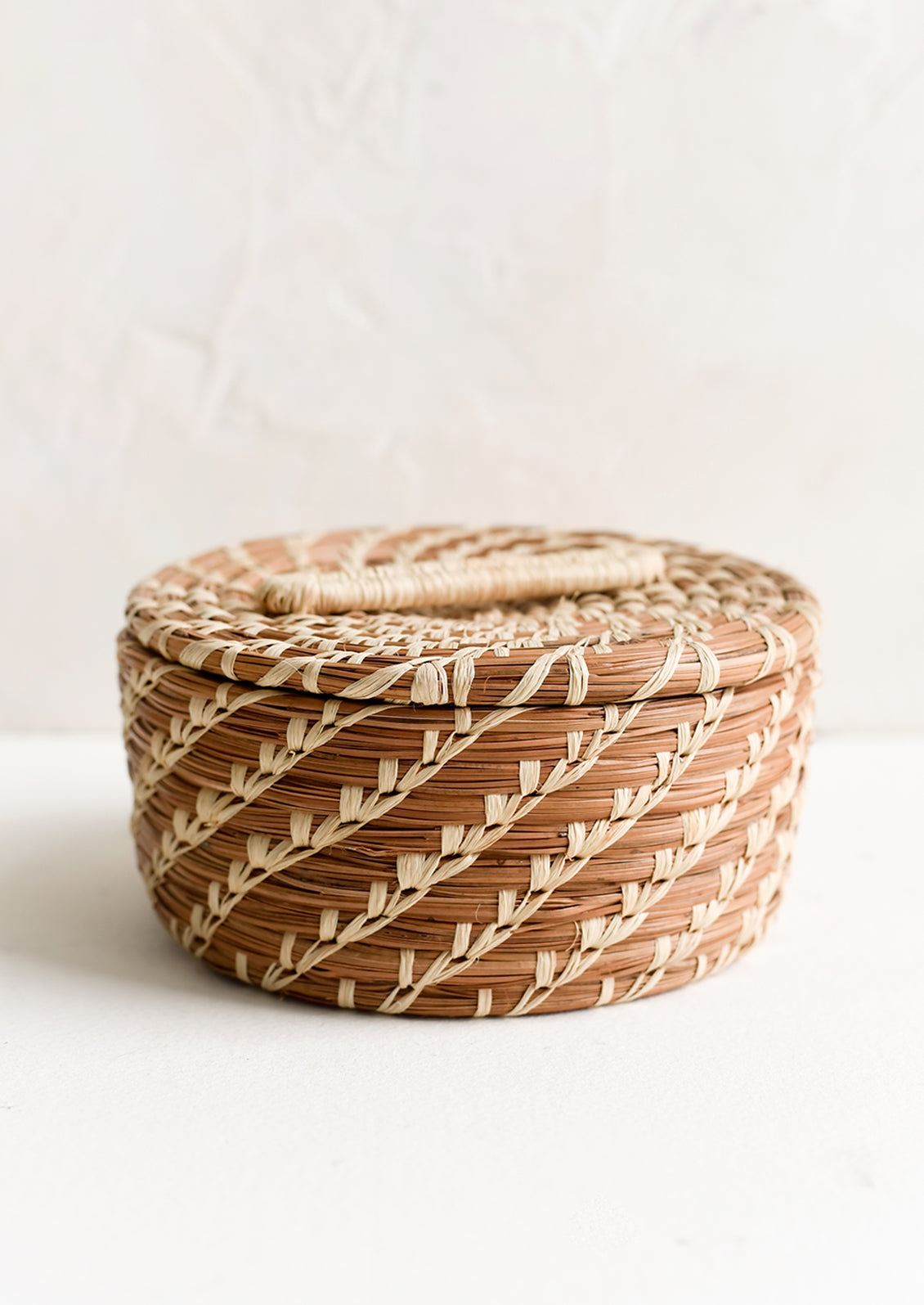 A small, round lidded basket made from woven pine needles.