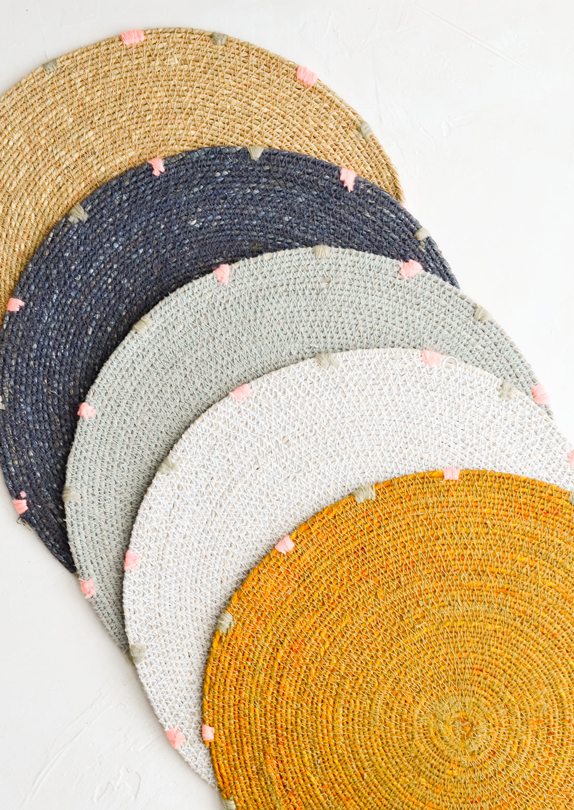 Five round seagrass placemats in assorted colors.