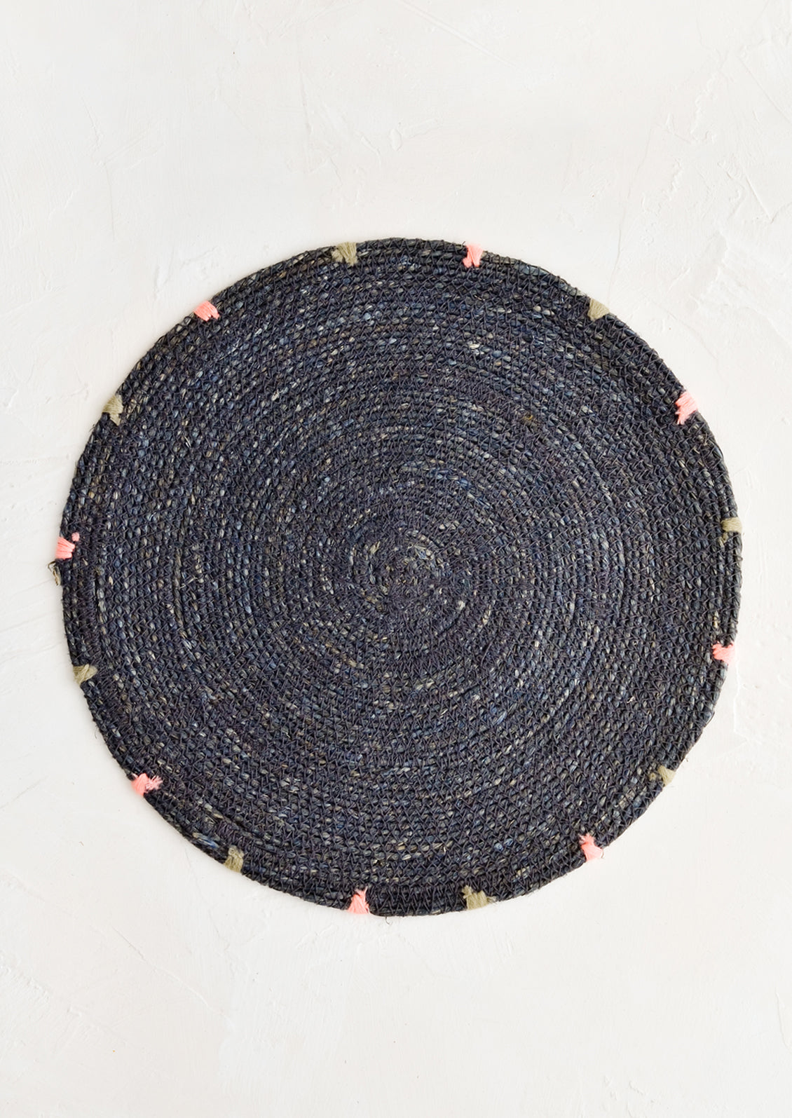 A round seagrass placemat in navy with grey and pink dashes embroidered around rim.