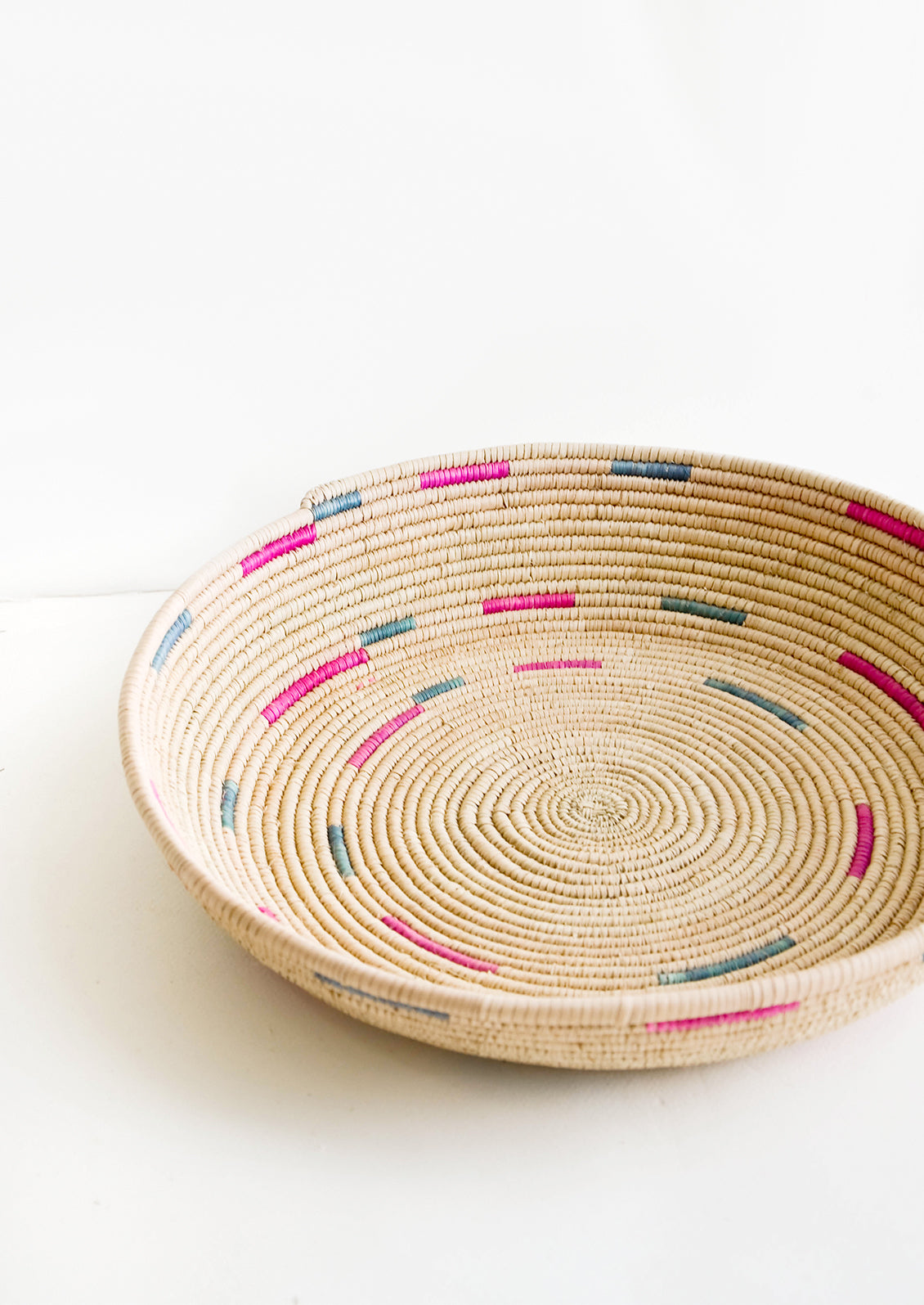 Woven platter made from date palm with pink and green design
