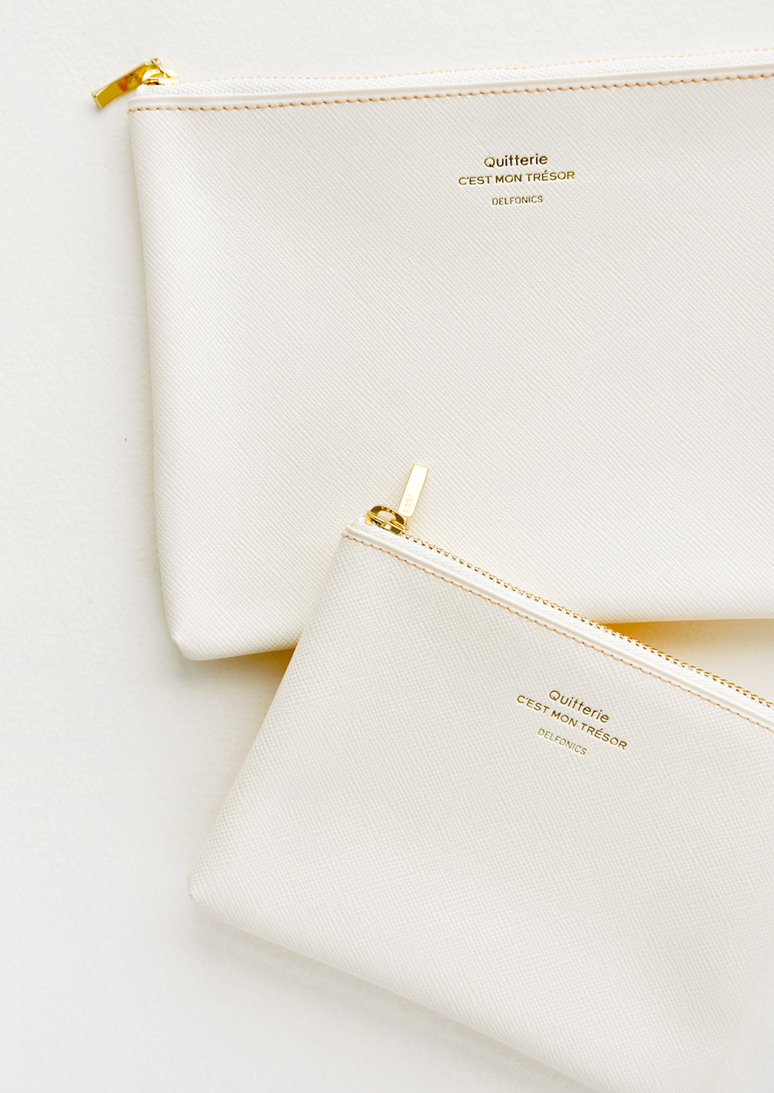 Medium and small vinyl pouches with gold zipper and crosshatch texture, in cream.