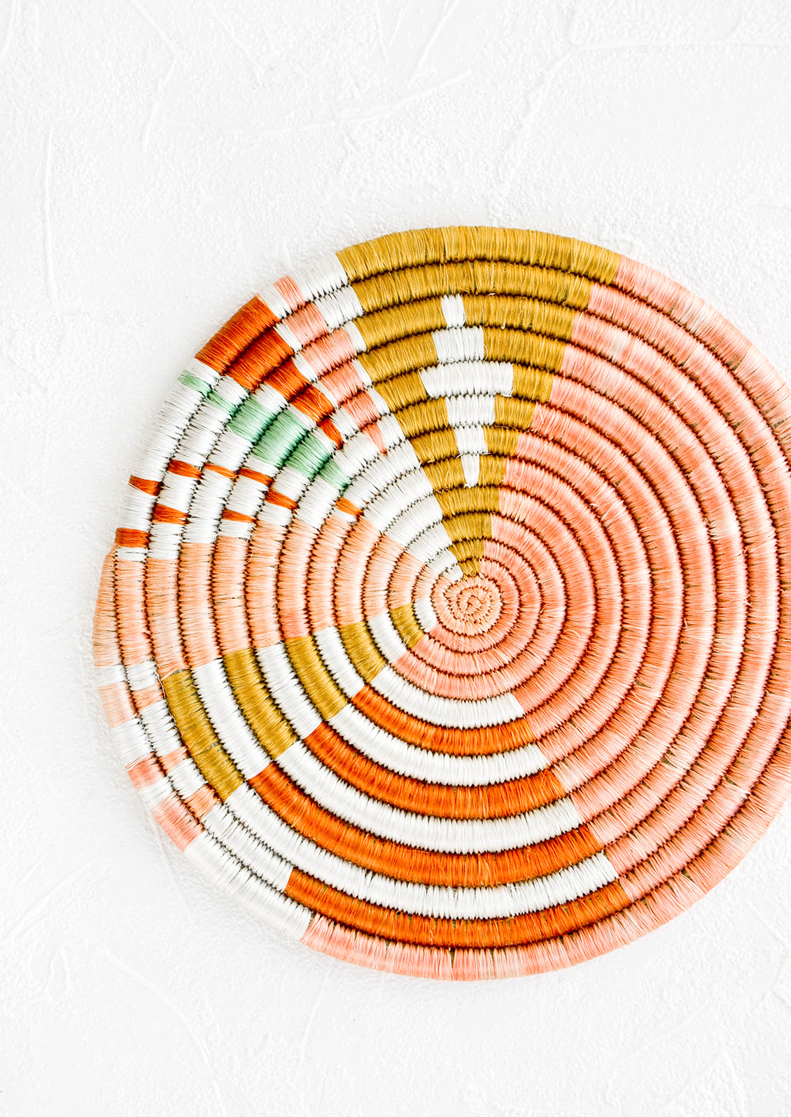 Colorful round trivet made from dyed raffia in a geometric pattern and pastel hues